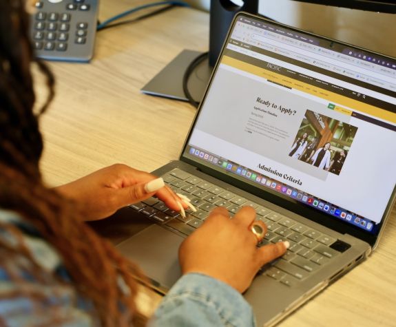 A woman is sitting in front of a laptop and looking at Pacific's DMSc/DHSc application page